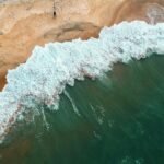 pexels-photo-982263-982263 Aerial shot of ocean waves crashing onto a sandy beach with two people in the distance.